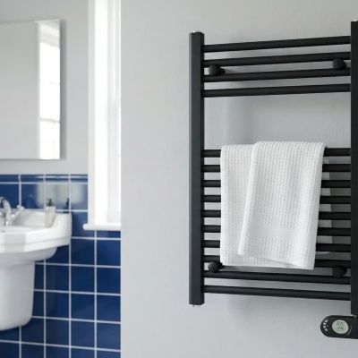 Radiador toalheiro preto com toalha branca numa casa de banho com lavatório e azulejos azuis.