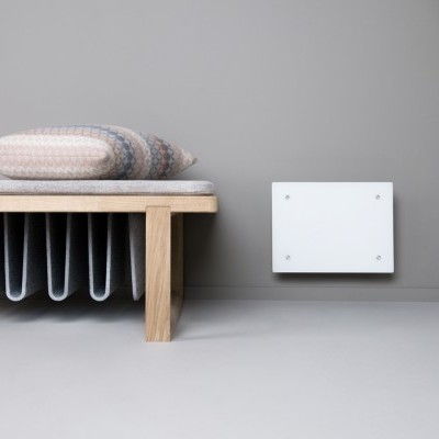 Banco de madeira clara com almofada e manta cinzenta junto a parede cinzenta com placa branca