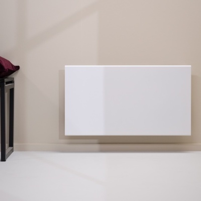 Radiador elétrico branco instalado numa parede bege com banco preto e almofada vermelha escura ao lado