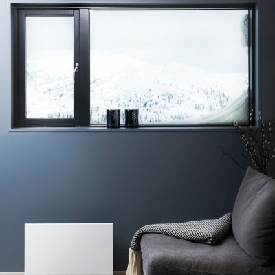 Janela preta de alumínio com vista nevada, sofá cinzento com manta, aquecedor branco e parede azul escura