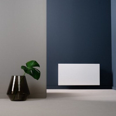 Radiador branco montado na parede azul com vaso de vidro escuro e folha verde no chão