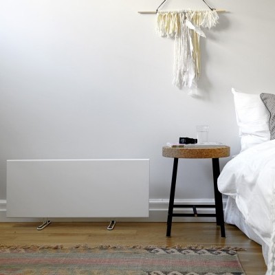 Radiador branco moderno junto a cama com roupa branca e mesa de madeira