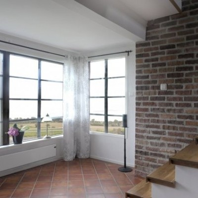 Espaço interior com janela grande, cortinas brancas, parede em tijolo e escada de madeira