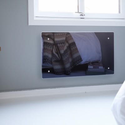 Painel decorativo triangular escuro refletor fixado na parede cinzenta de uma divisão interior com janela branca