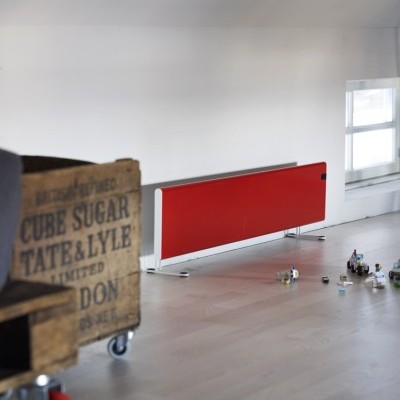 Carrinho de madeira com inscrições, divisória vermelha e latas no chão em sala clara