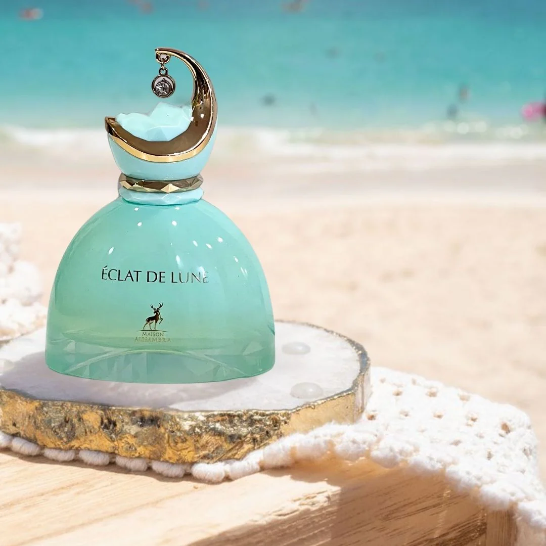 Frasco de perfume verde água com tampa dourada em forma de lua sobre pedra na praia