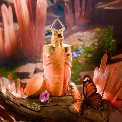 Frasco de perfume rosa metálico com tampa dourada decorada com borboleta e borboleta real ao lado