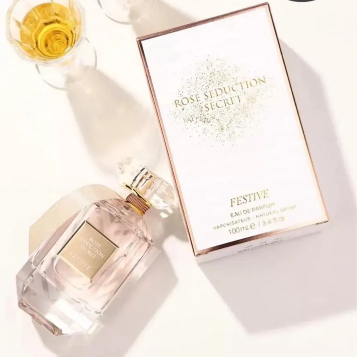 Frasco de perfume Rose Seduction Secret e caixa branca com texto em dourado ao lado de um copo com líquido amarelo