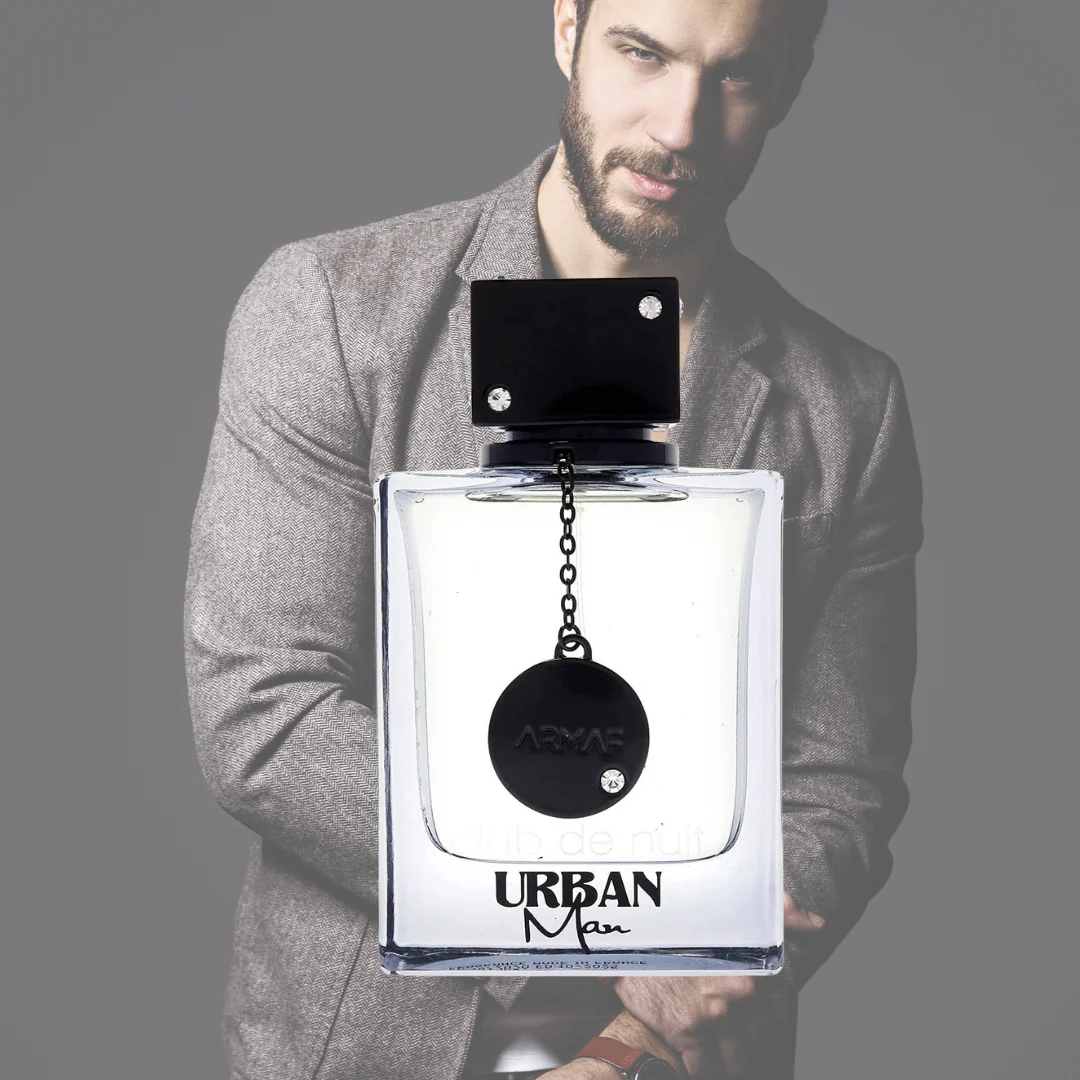 Frasco de perfume URBAN Man com tampa preta e medalha pendurada, homem barbudo ao fundo desfocado.