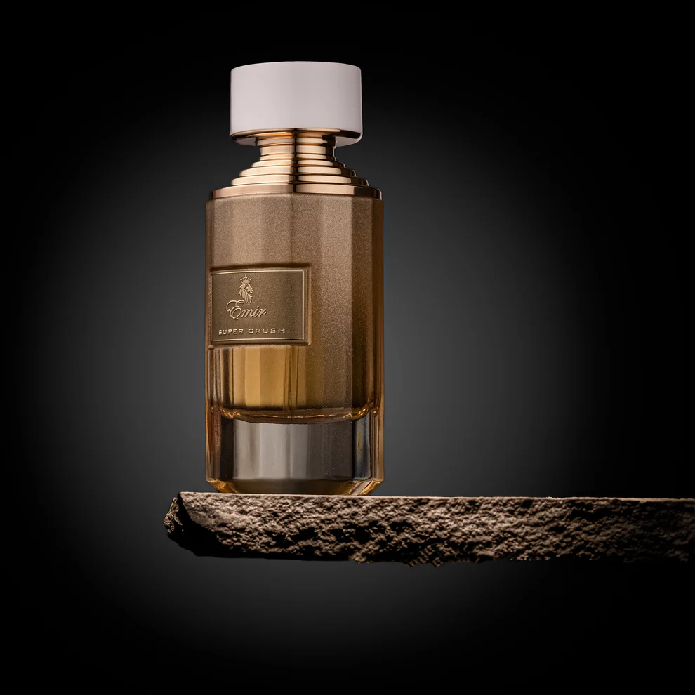 Frasco de perfume castanho com tampa branca e dourada sobre superfície rústica