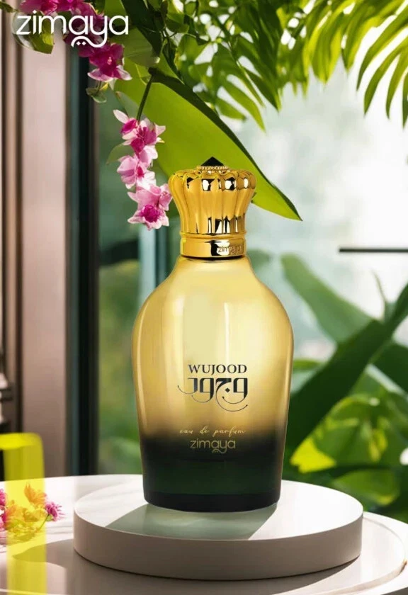 Garrafa de perfume dourada e preta com tampa dourada ornamental, em suporte branco com plantas ao fundo.