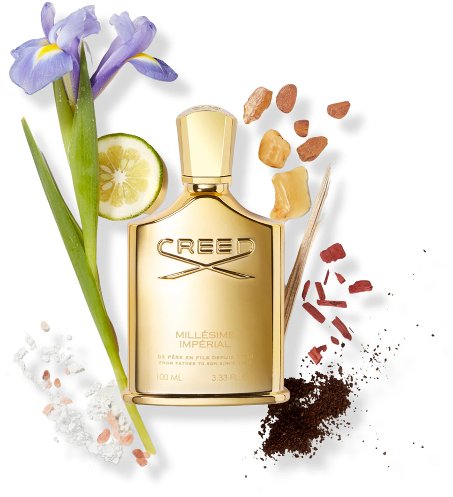 Frasco dourado de perfume Creed com ingredientes naturais ao redor.