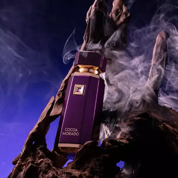 Frasco de perfume roxo escuro com detalhes dourados e fumo em fundo azul escuro