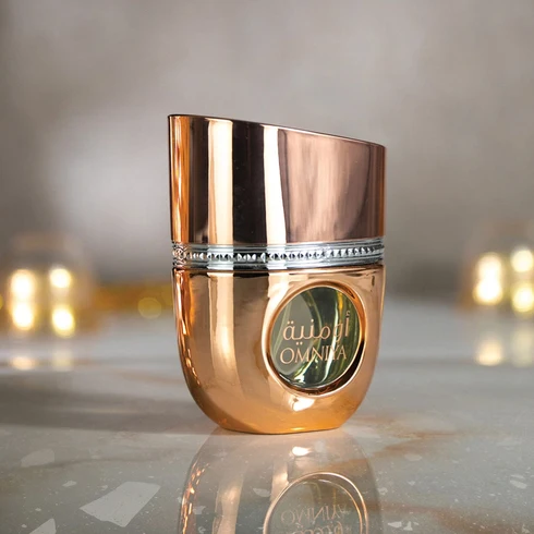 Frasco de perfume dourado metálico com tampa assimétrica e etiqueta redonda verde