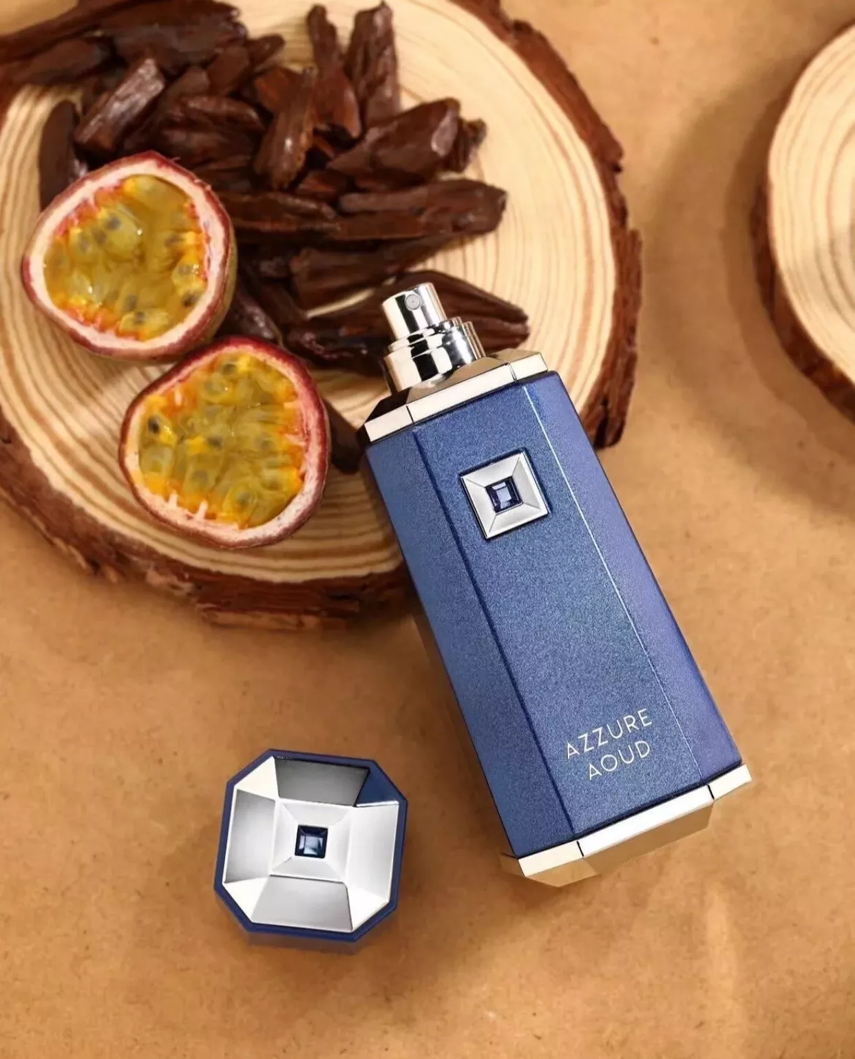 Frasco de perfume azul e prata com tampa ao lado sobre fundo castanho e disco de madeira com maracujá