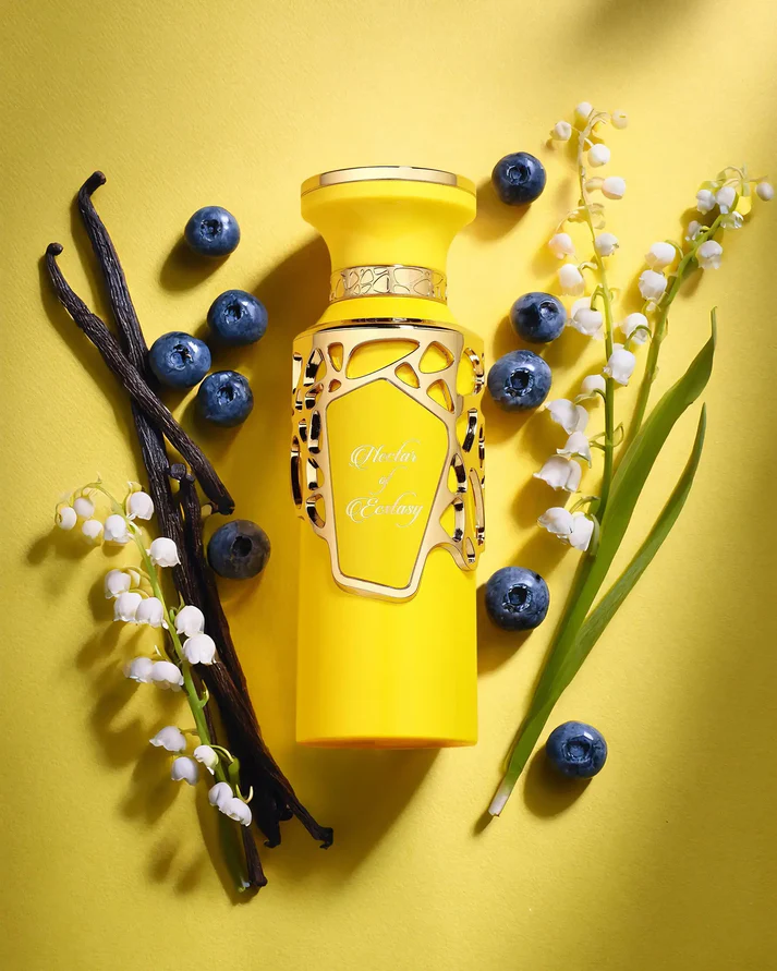 Frasco amarelo de perfume com detalhes dourados e texto Violet & Ecstasy com bagas azuis e flores brancas em fundo amarelo