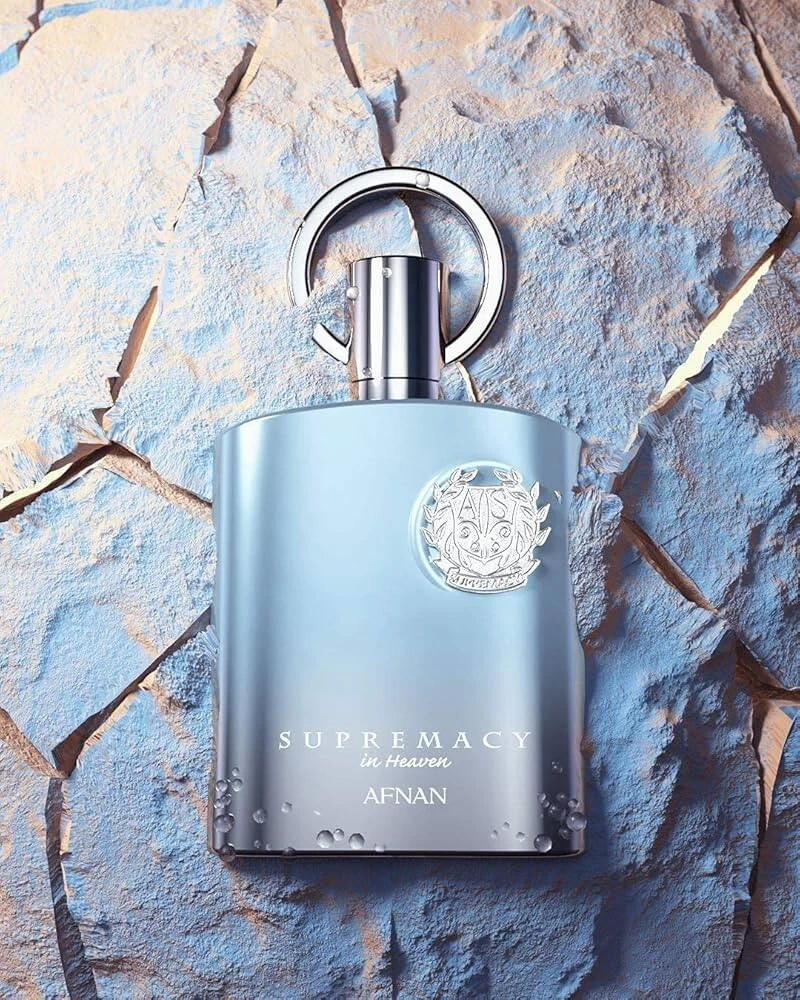 Frasco de perfume azul metálico com símbolos e texto em relevo sobre fundo rochoso azul e castanho