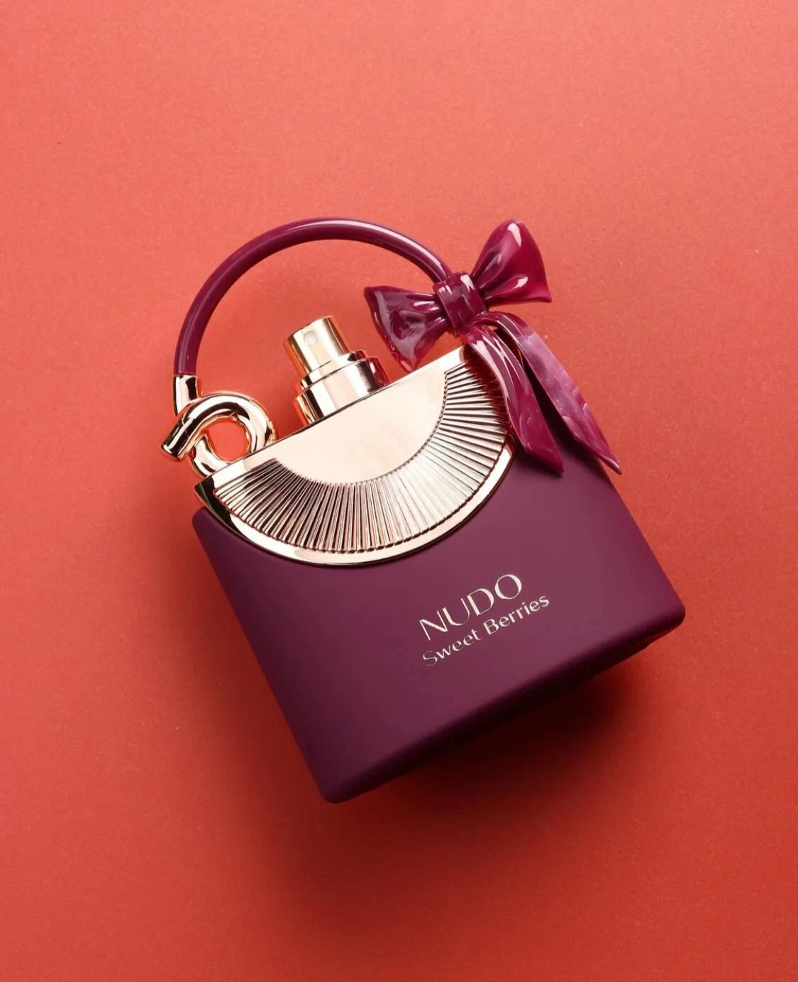 Frasco de perfume roxo com tampa dourada e laço roxo.