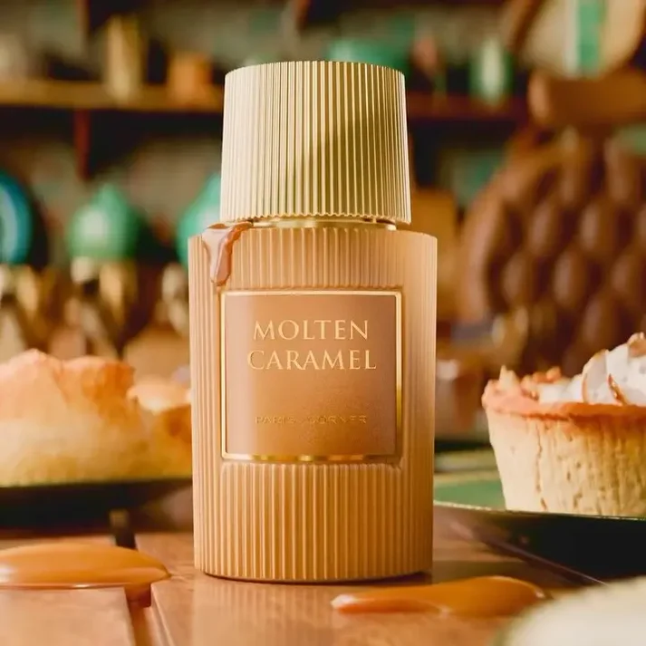 Frasco dourado com rótulo MOLTEN CARAMEL em mesa de madeira com caramelo derramado