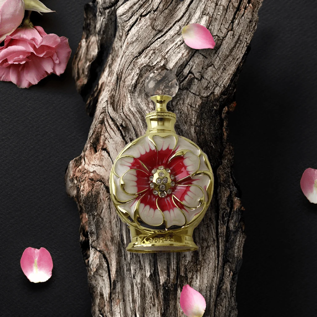 Frasco de perfume decorativo dourado com flor vermelha e branca sobre madeira e pétalas de rosa