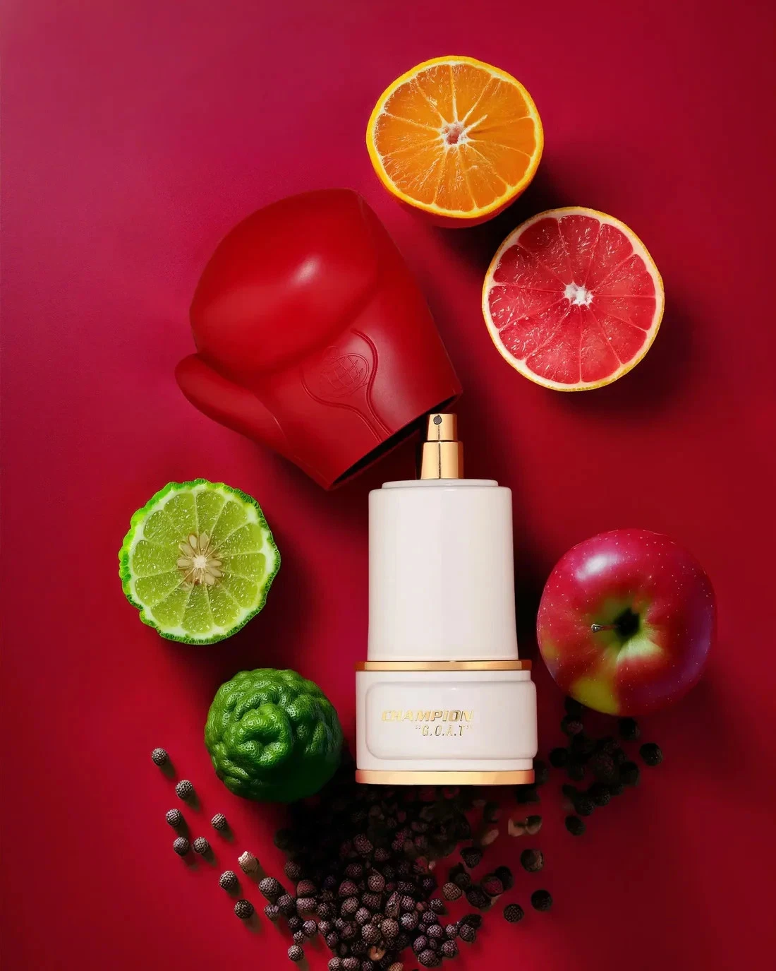 Frasco branco com tampa dourada, luva de boxe vermelha, frutas cítricas cortadas e maçã sobre fundo vermelho