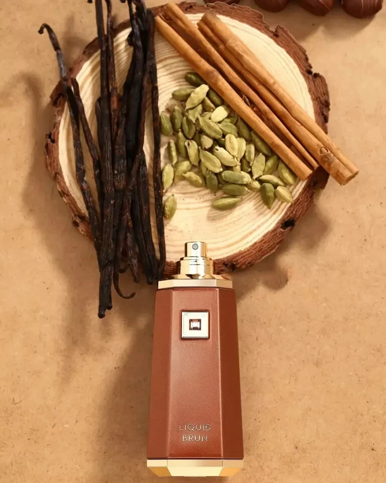 Frasco de perfume com vagem de baunilha, paus de canela e sementes verdes sobre suporte de madeira.