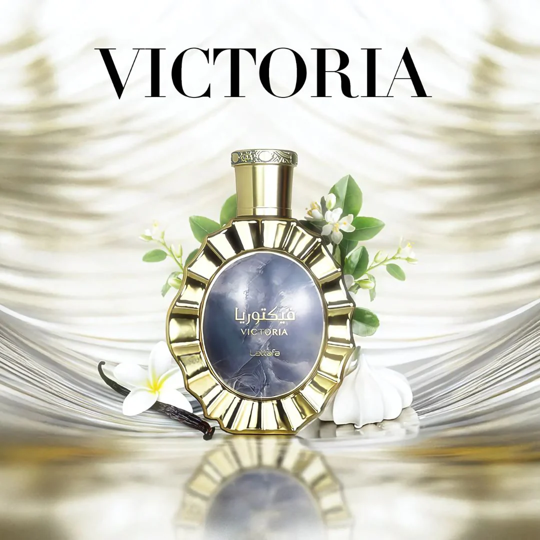 Frasco de perfume dourado Victoria com flores brancas e folhas verdes ao fundo