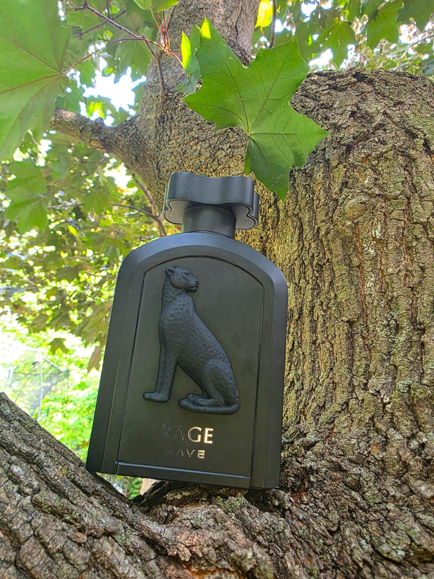 Frasco preto de perfume com relevo de leopardo sobre casca de árvore e folhas verdes ao fundo