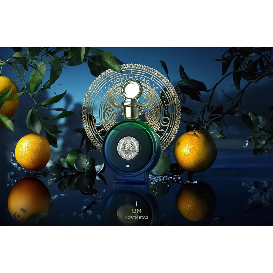 Frasco de perfume verde escuro com tampa dourada e laranjas ao redor num cenário azul escuro