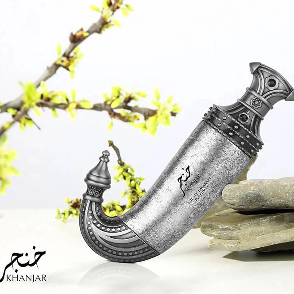 Adaga tradicional com bainha curva e cabo decorativo apoiada em pedras com ramos verdes ao fundo