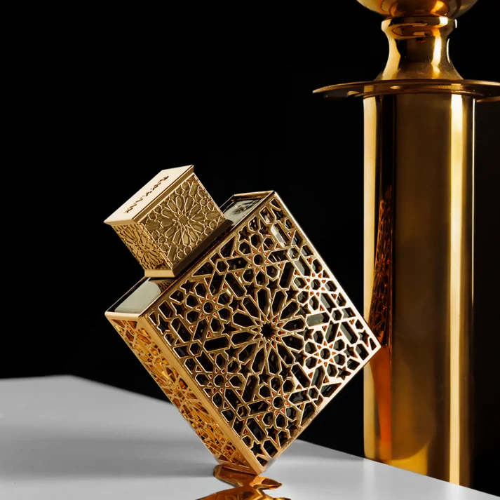 Frasco de perfume decorativo dourado com padrão geométrico e tampa elaborada