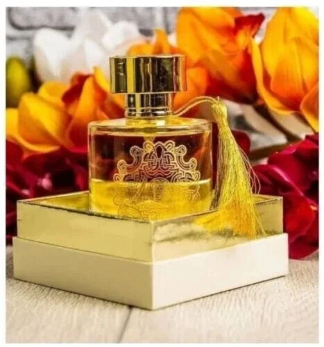 Frasco de perfume dourado com tassel em caixa dourada e branca e flores ao fundo