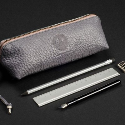 Estojo cinza rugoso com régua, lápis, caneta tinteiro e clipe sobre fundo preto