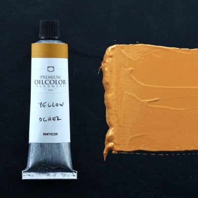 Tubo de tinta de óleo amarelo ocre com amostra da tinta numa superfície preta