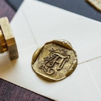 Envelope branco com selo de lacre dourado com letra A e selo de madeira ao lado