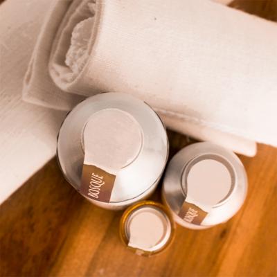 Frascos metálicos com etiquetas 'BOSQUE' sobre superfície de madeira e tecido branco