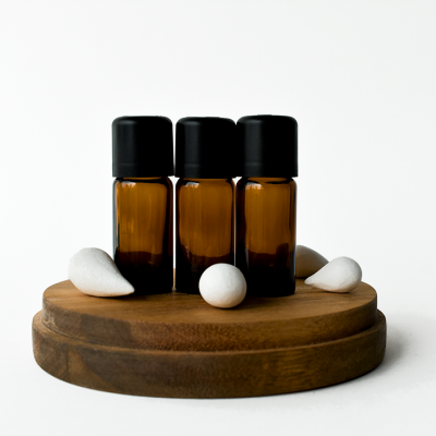 Três frascos âmbar com tampas pretas sobre base de madeira com pedras brancas