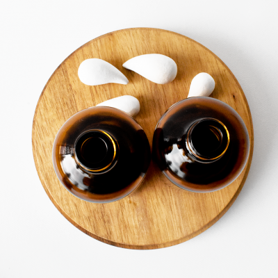 Duas garrafas de vidro castanho sobre tábua redonda de madeira com quatro pedras brancas