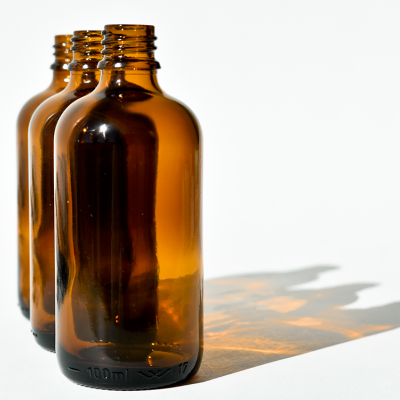 Três frascos de vidro âmbar com capacidade 100 ml alinhados sobre fundo branco.