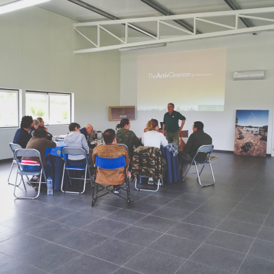 Sala ampla com pessoas em cadeiras e projetor a mostrar texto