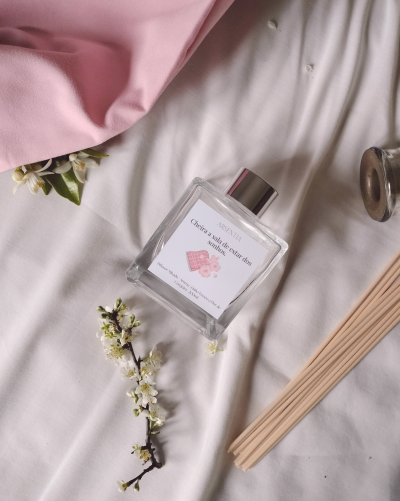 Frasco de vidro de difusor de ambiente com etiqueta sobre tecido branco e rosa com flores e varetas