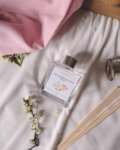 Difusor de aroma em frasco de vidro sobre superfície branca com pauzinhos e ramo de flores