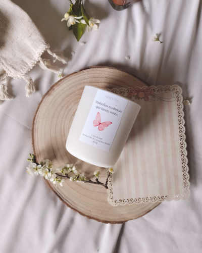 Vela aromática branca com etiqueta sobre base de madeira com flores e guardanapo rendado