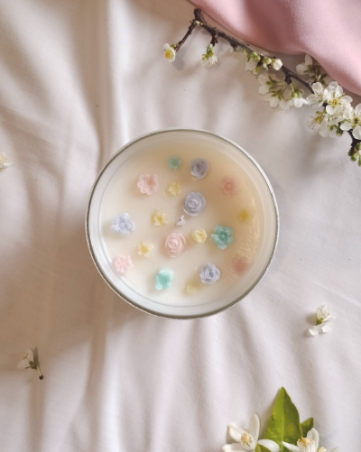 Vela artesanal com flores coloridas em vidro sobre tecido branco