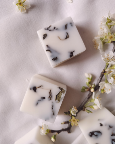 Sabonetes brancos com folhas secas sobre tecido branco com flores.