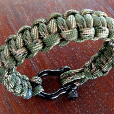 Pulseira trançada de paracord verde e bege com fecho preto sobre madeira.