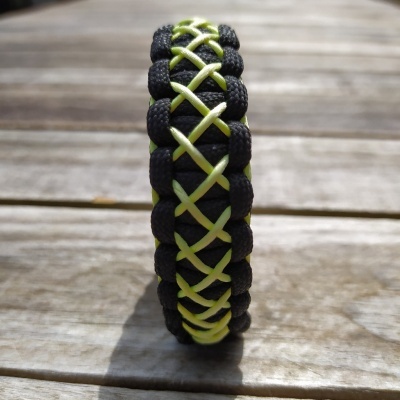 Pulseira trançada preta e verde-limão sobre madeira clara