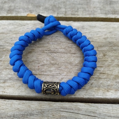 Pulseira trançada azul com detalhe metálico sobre madeira
