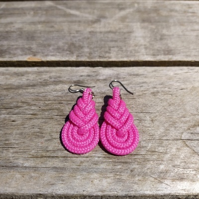 Brincos pendentes de corda rosa trançada sobre madeira