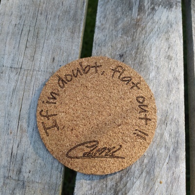 Porta-copos redondo de cortiça com frase motivacional em inglês sobre madeira envelhecida